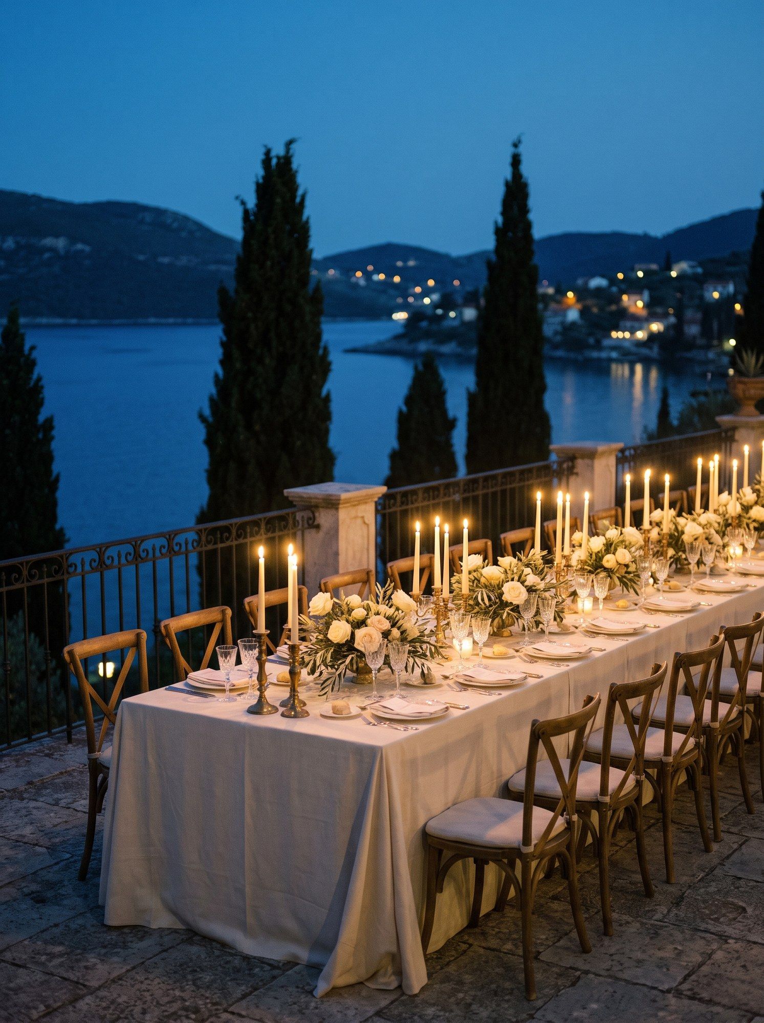 A candlelit terrace table above a Mediterranean bay at blue hour